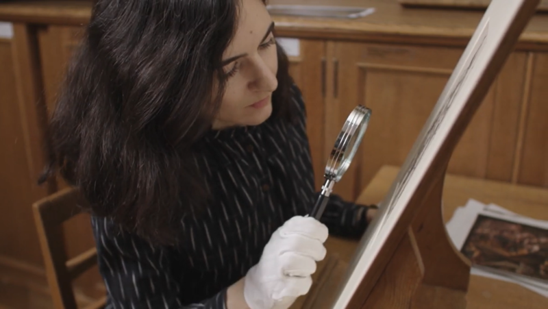 A woman uses a magnifying glass to look at artworks in the Ashmolean's Western Art Print Room